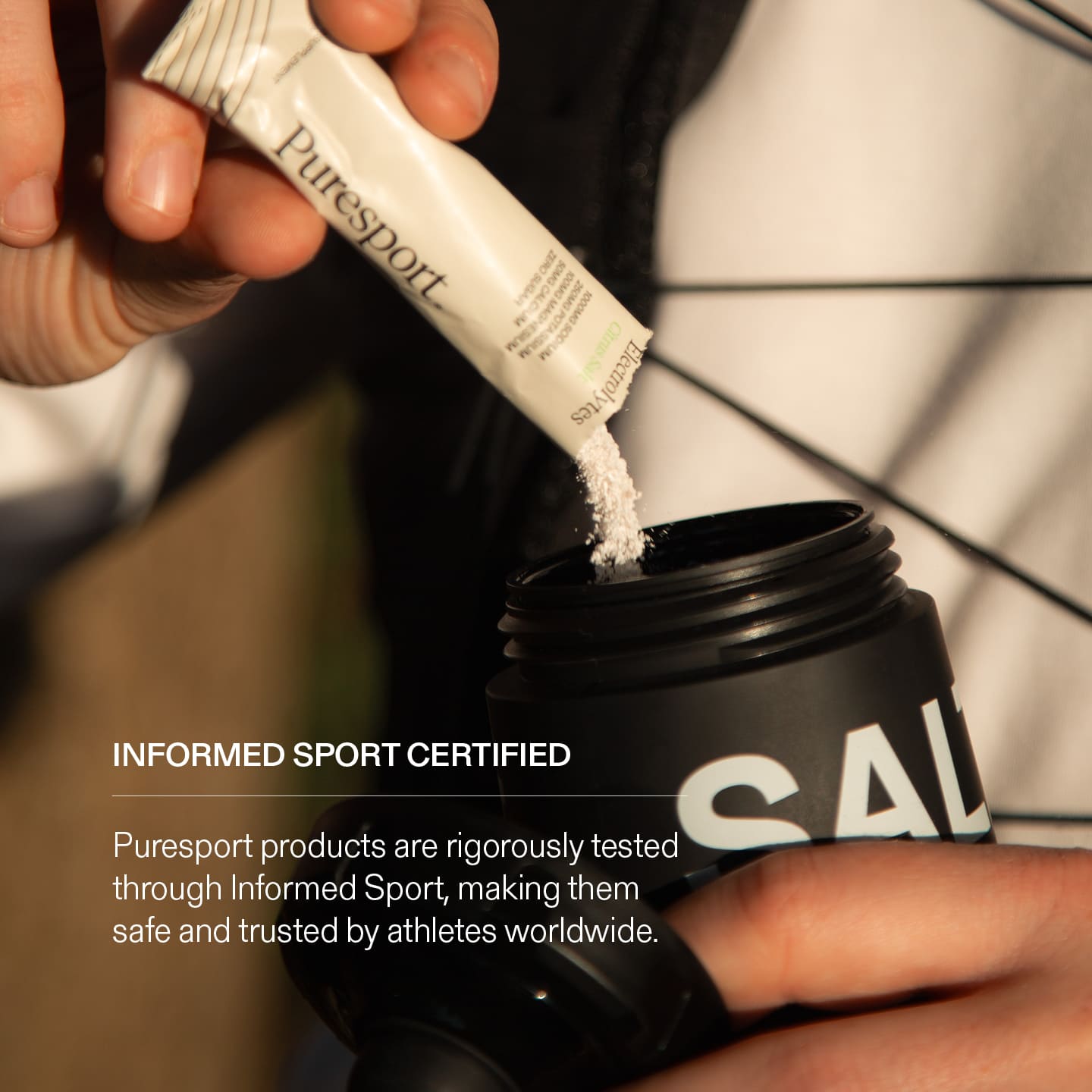 Person pouring a electrolyte poweder from a Puresport sachet into a black sports bottle with Informed Sport Certified Badge.
