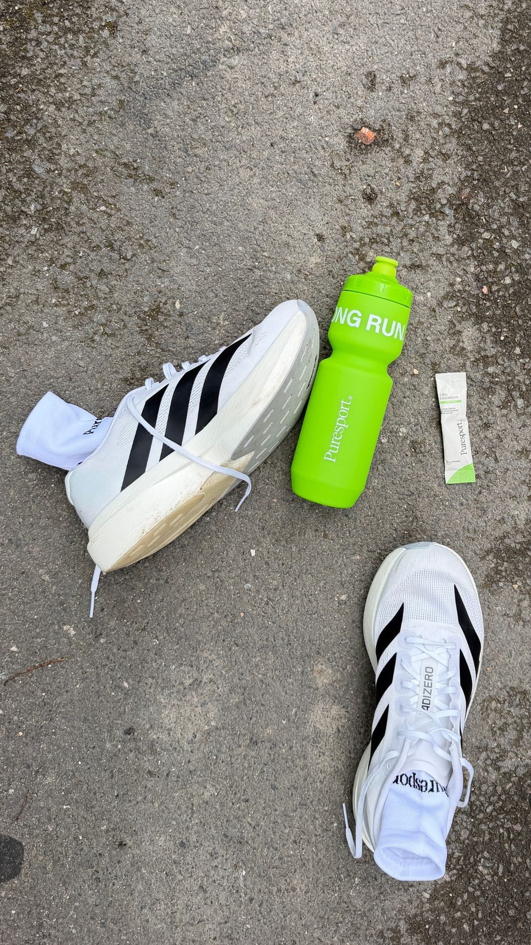 White Adidas evo SLs sneakers with black stripes and a green water bottle with Citrus salt electrolytes by Puresport. 