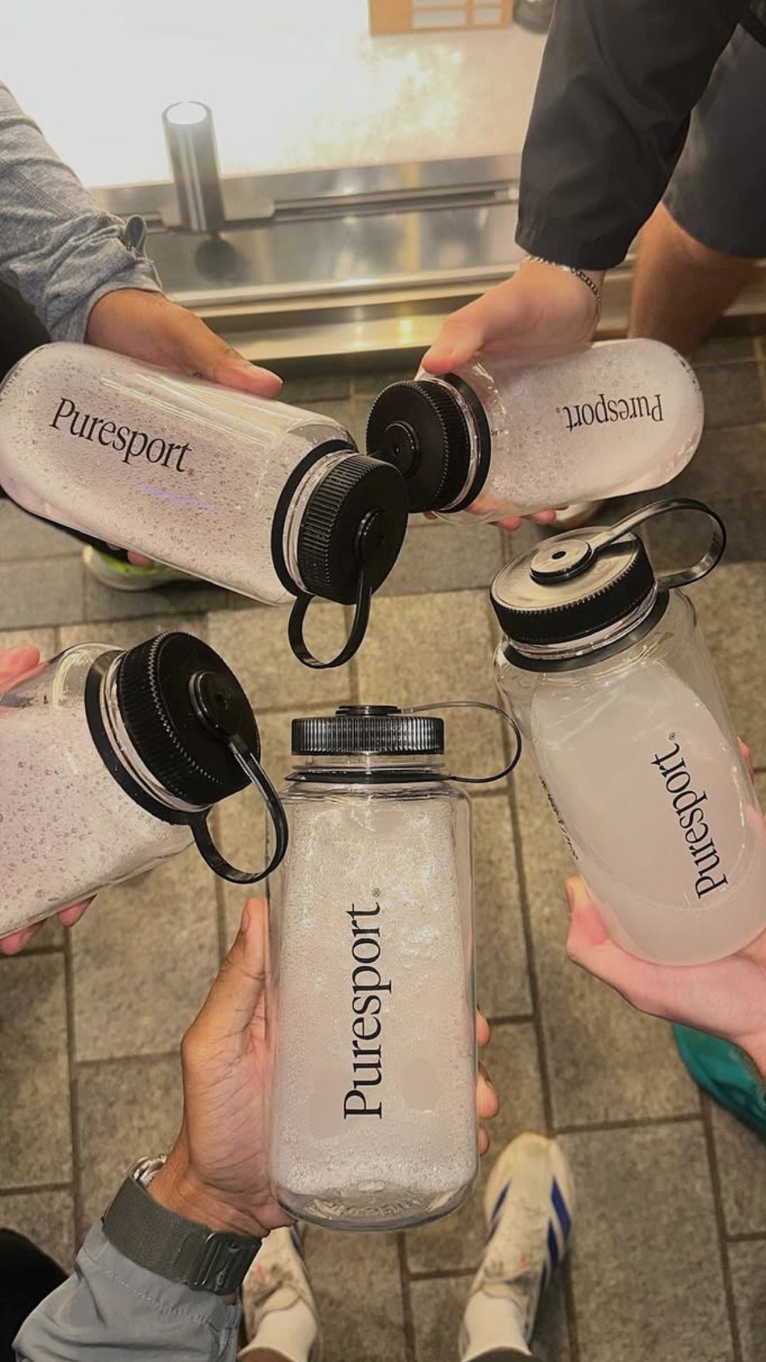 Multiple hands holding Puresport water bottles at a run club in London.