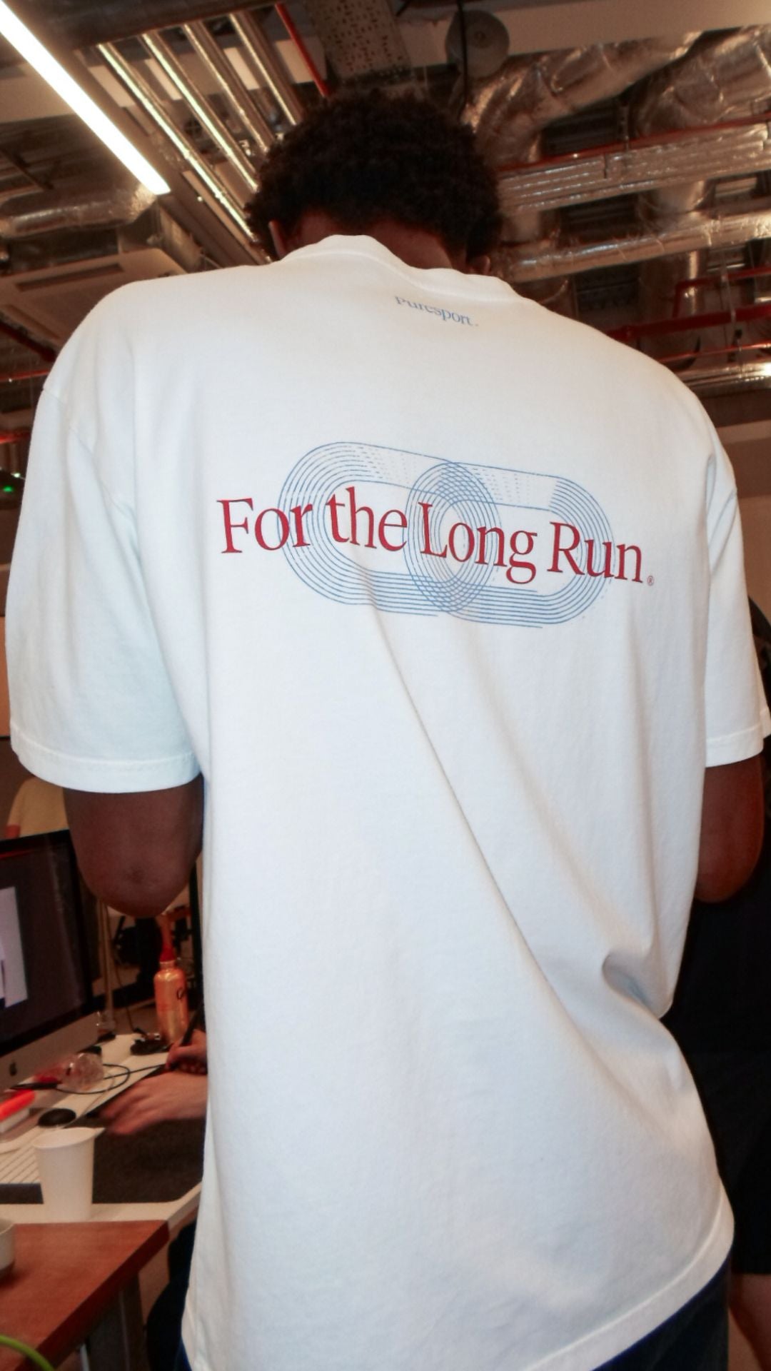 Person wearing a white t-shirt with 'For the Long Run' text in an indoor setting. 