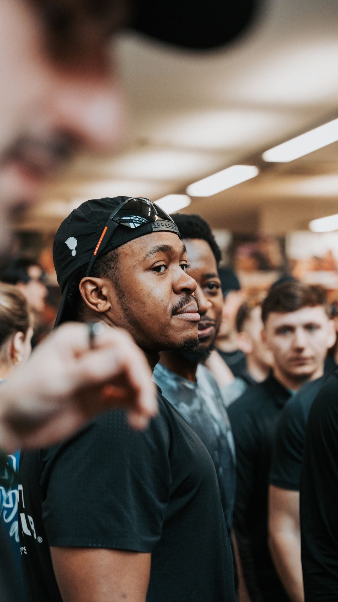 Man wearing a black Puresport cap and dark shirt in a crowded indoor run club setting