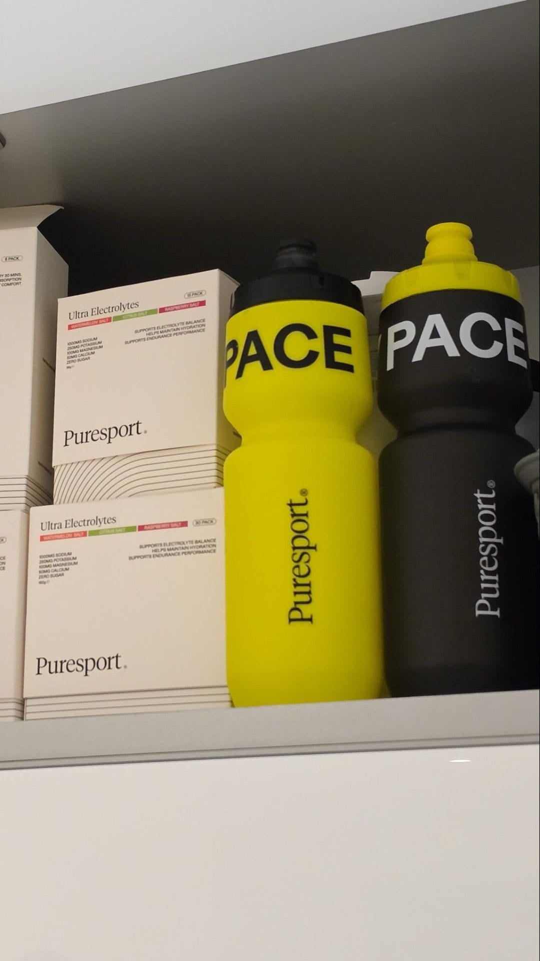 Two Puresport water bottles, one yellow and one black, on a shelf with Ultra Electrolytes. 