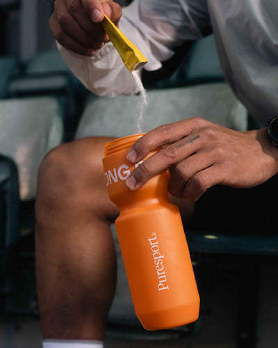 A male runner pouring electrolytes into a sports bottle. 