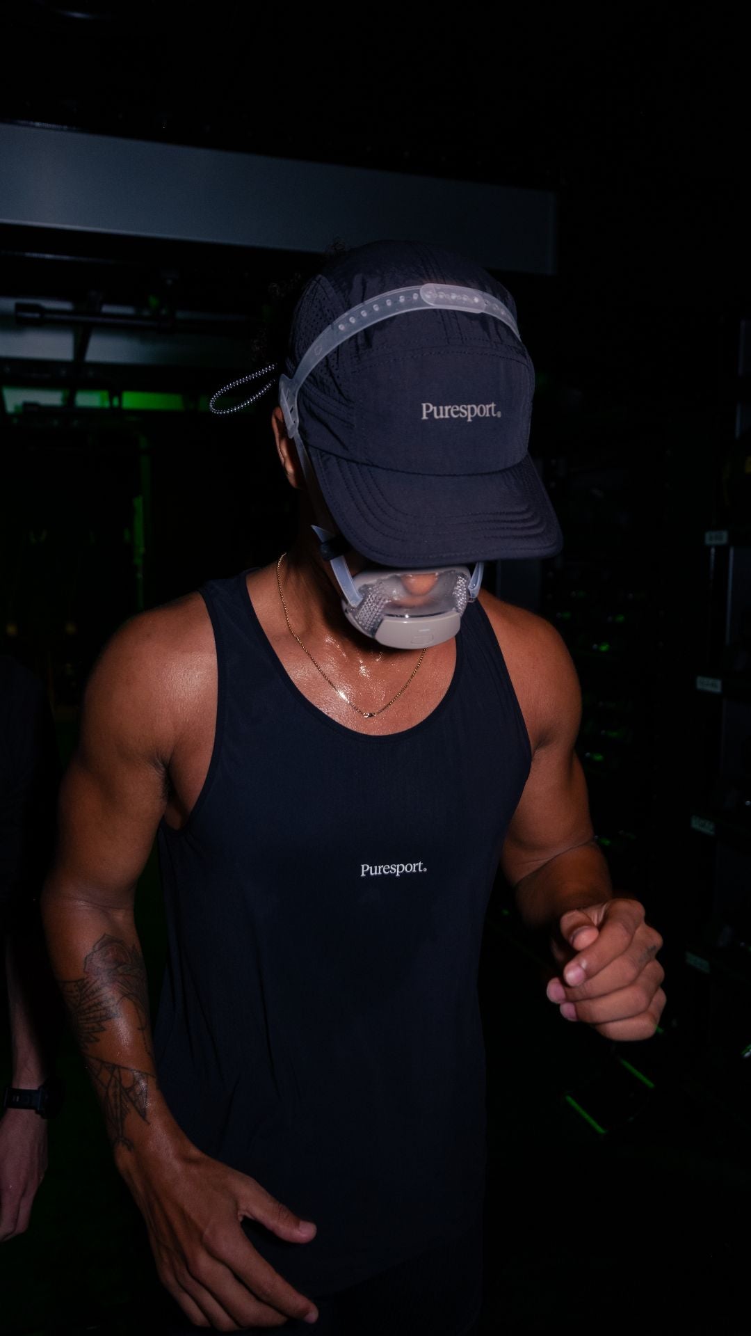 Runner wearing a black singlet and cap with 'Puresport' branding in a dark setting on a treadmill.