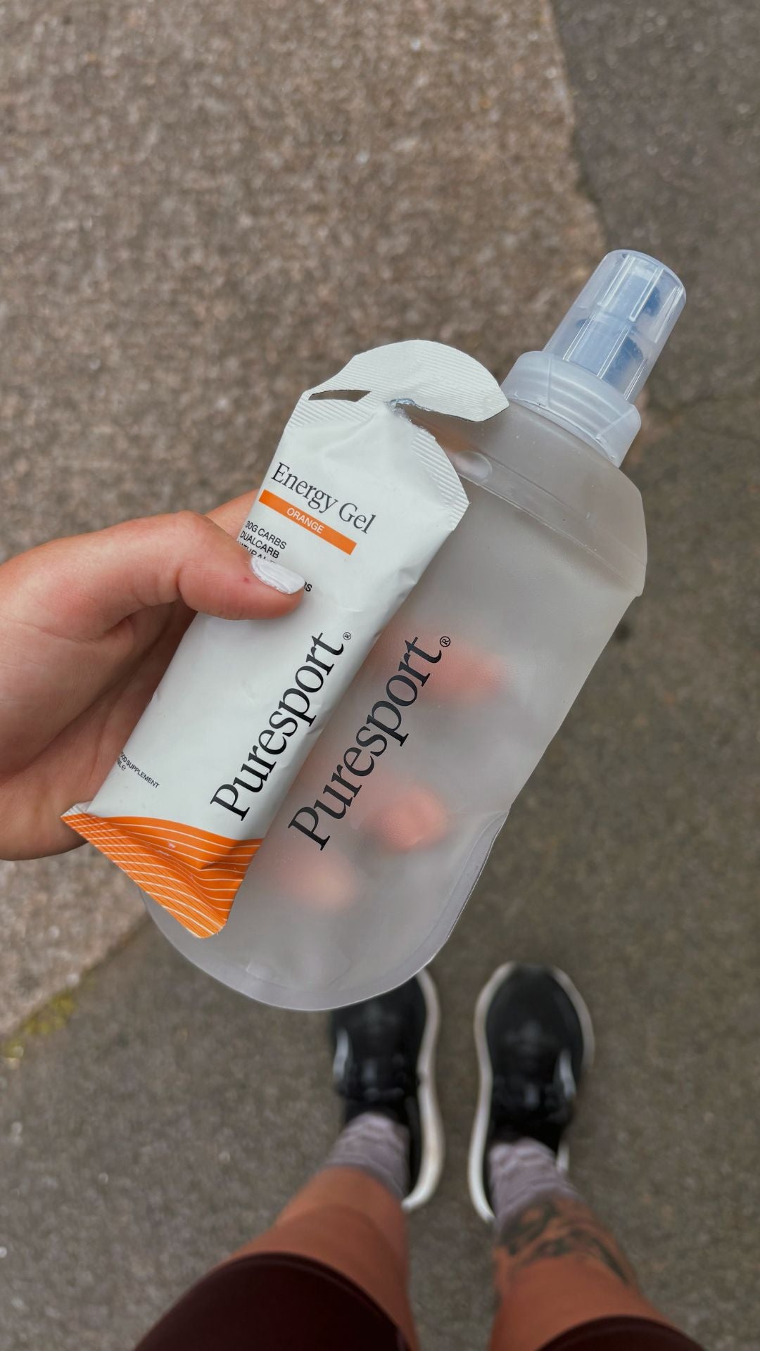 Puresport energy gel and flask bottle held by a runner on a concrete surface