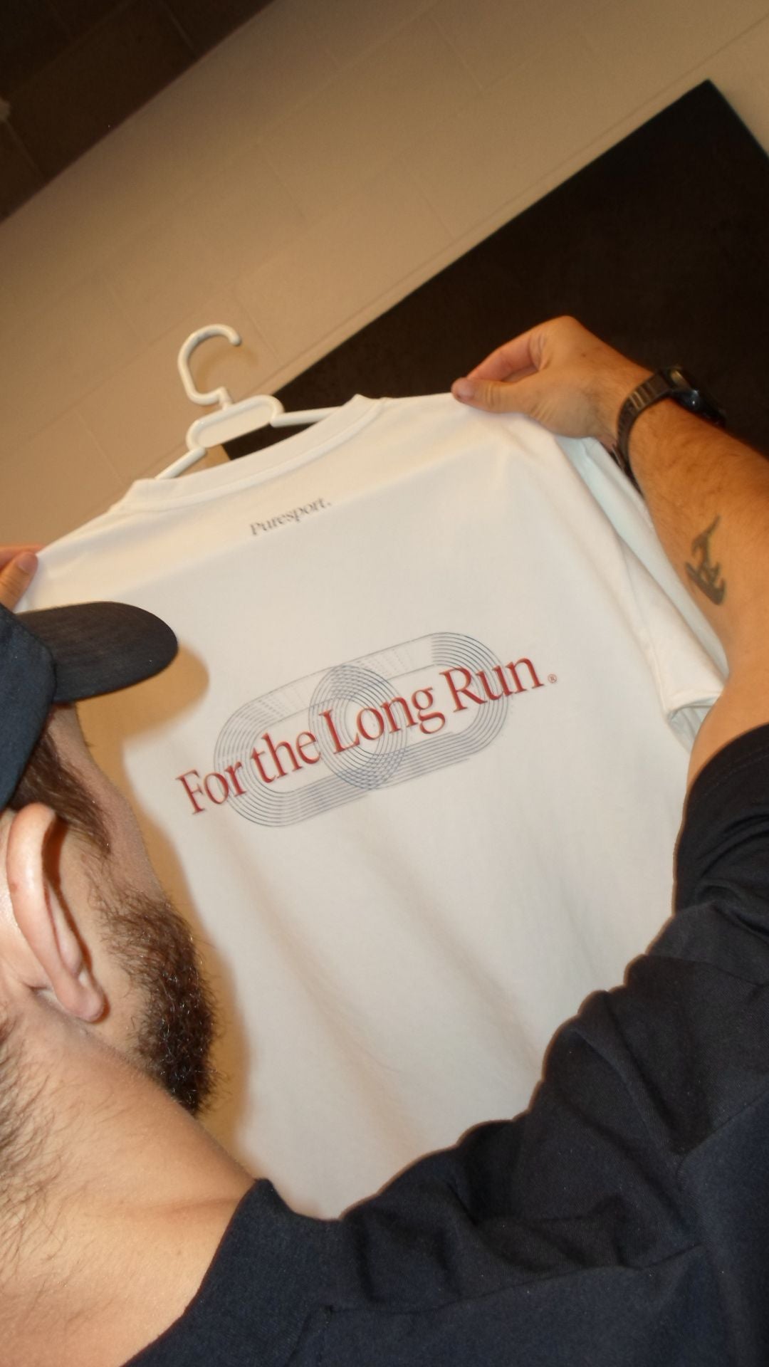 Male holding a white t-shirt with 'For the Long Run' text on a hanger at a photoshoot. 