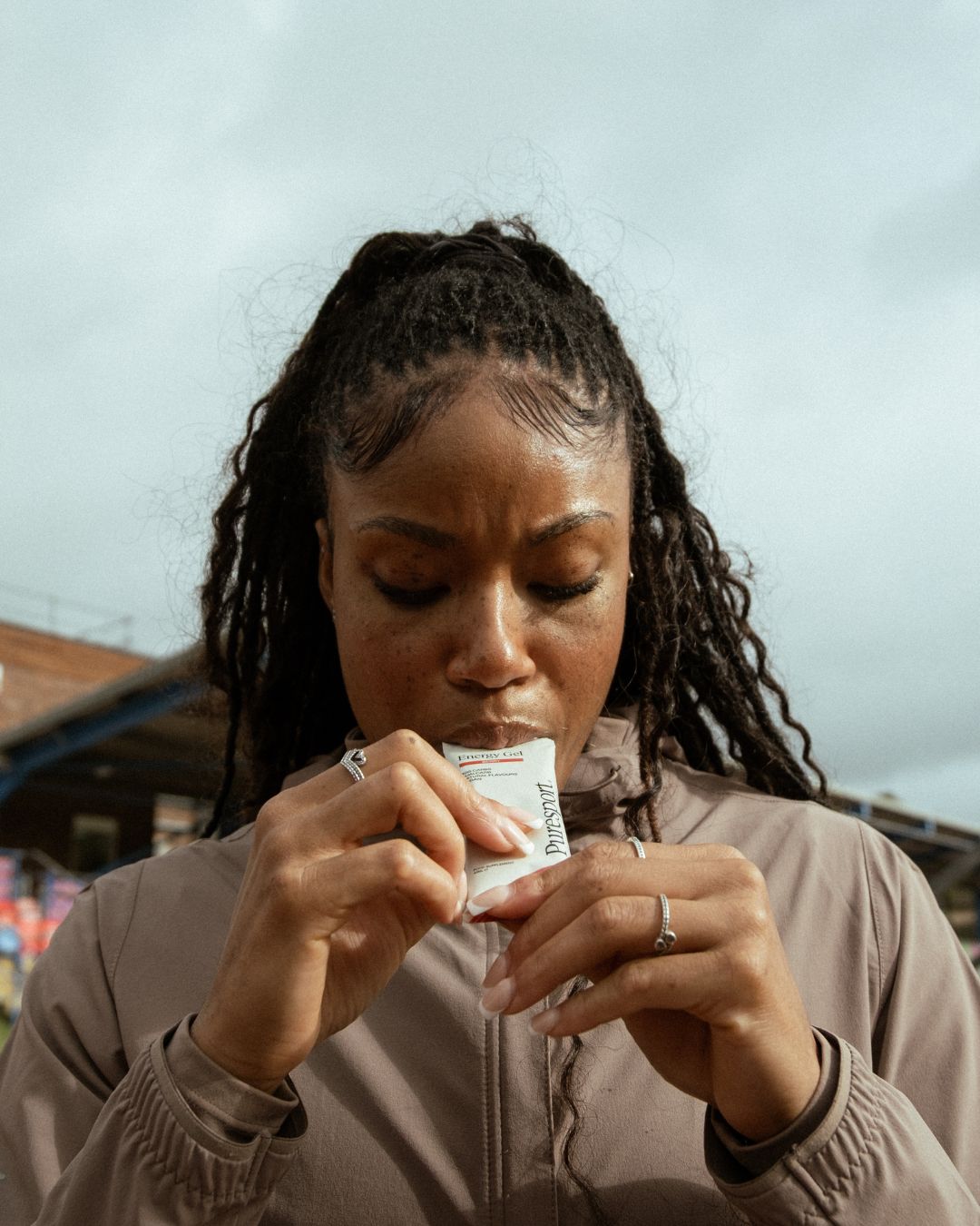 Women track athlete holding a Puresport energy gel close to their mouth against a blurred background
