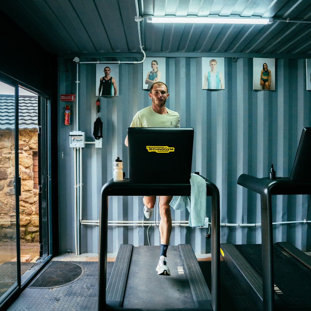 George Mills using a treadmill in a container-like structure with portraits on the wall.