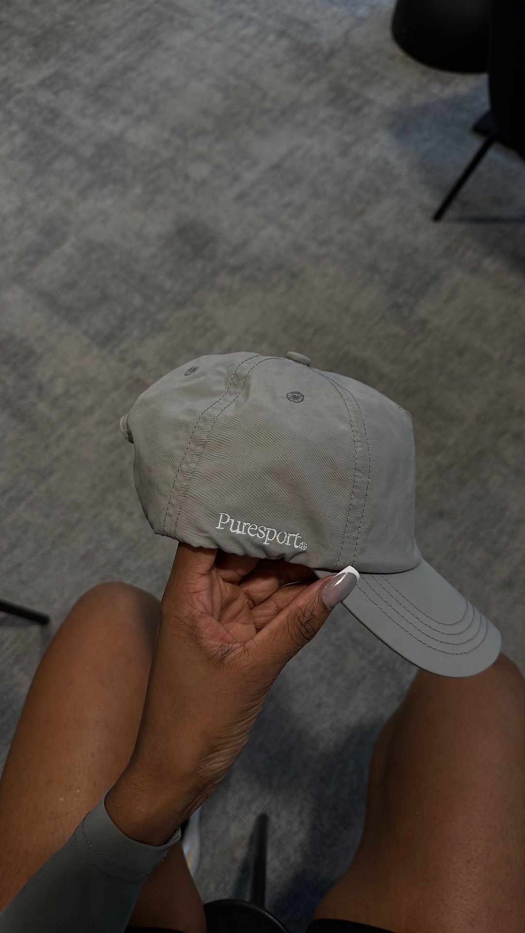 Person holding a grey running cap with 'Puresport' branding on a textured surface.