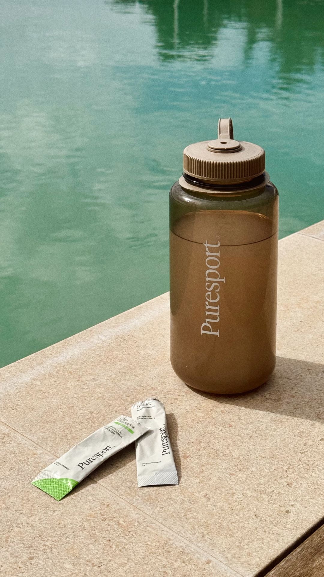 Puresport water bottle and sachet of electrolytes on a stone surface next to a pool. 