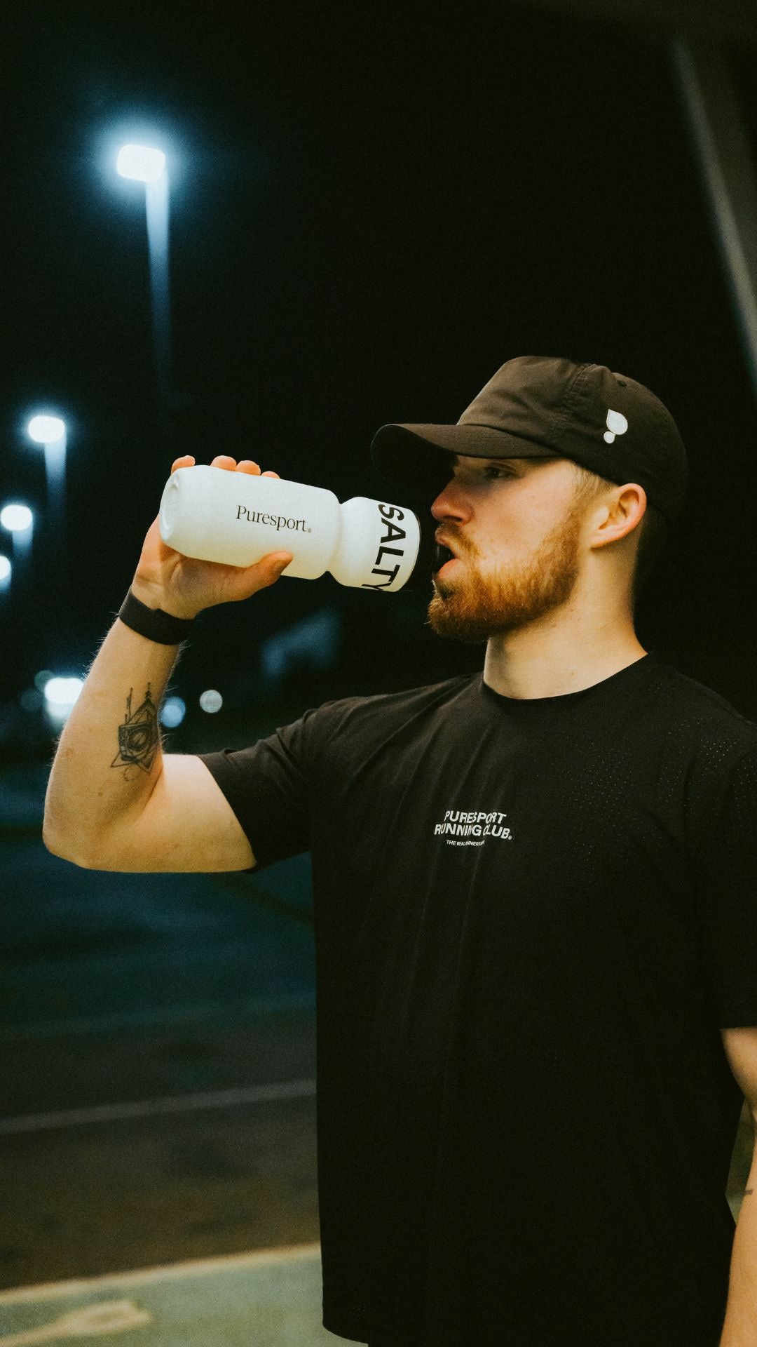 Man drinking from a Puresport bottle with text at night track session. 