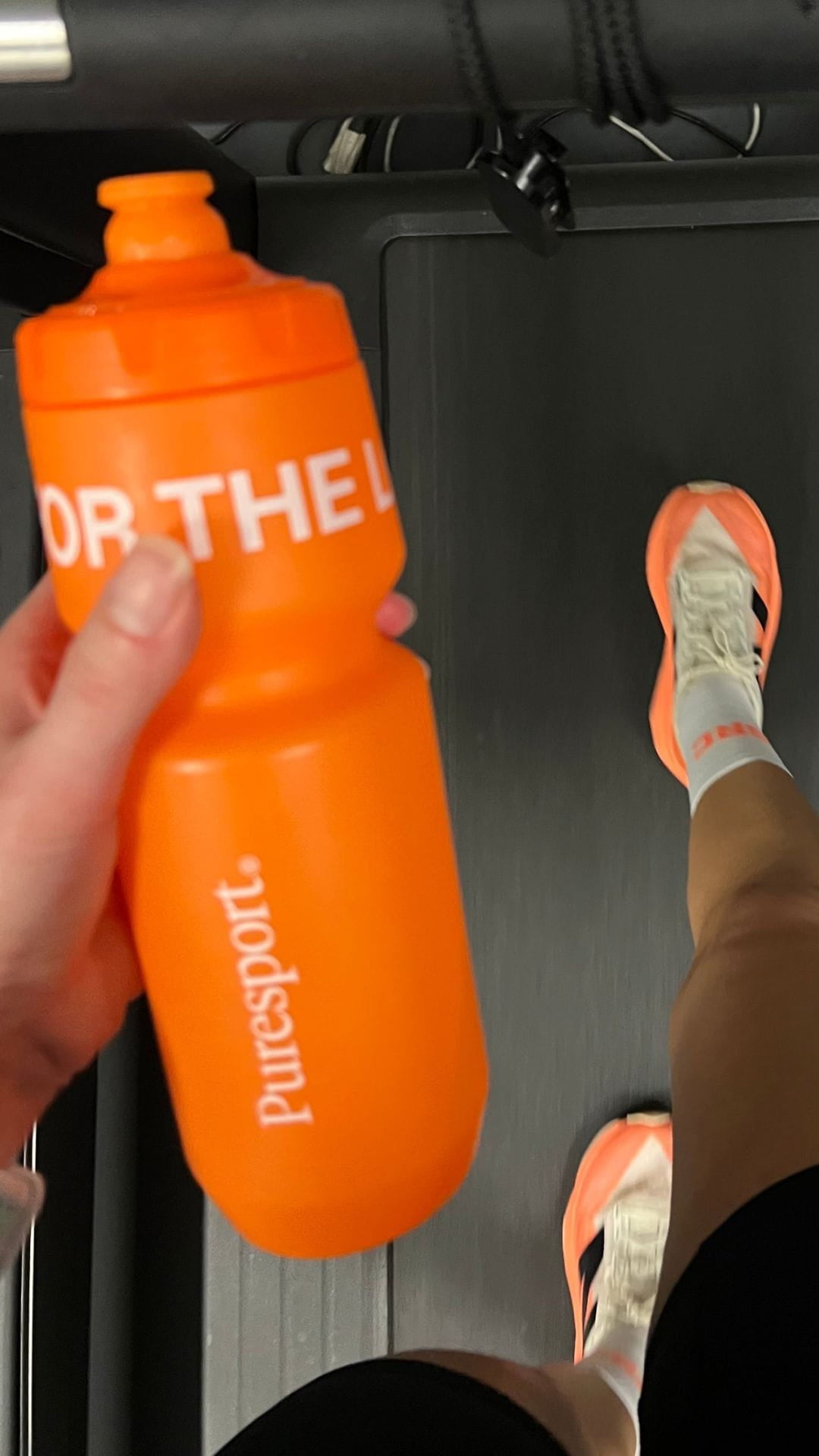 Orange sports bottle with 'Puresport' branding held by a person on. treadmill.