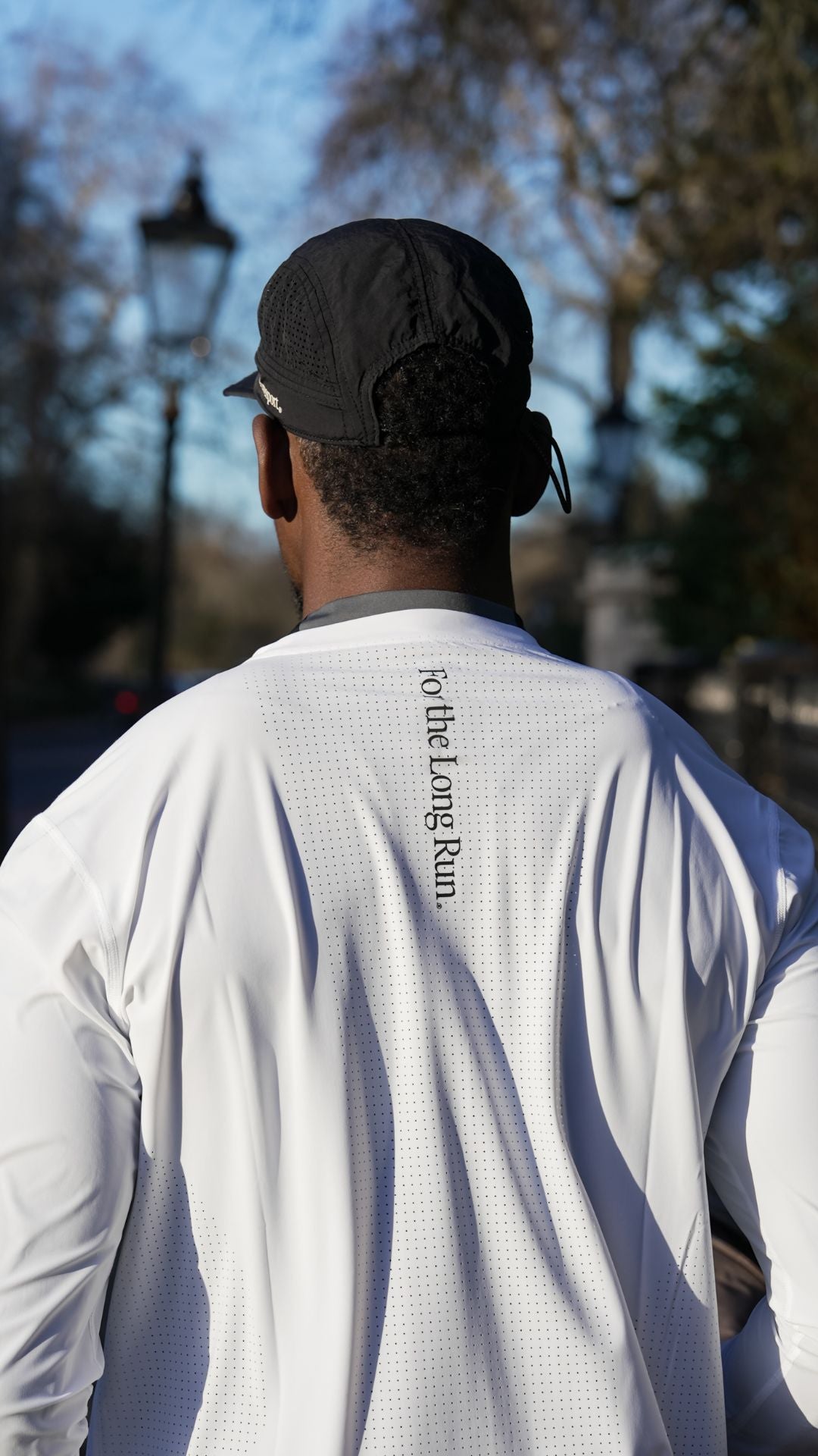 Runner wearing a white long-sleeve shirt with For the Long Run on the back, running around Dulwich park. 