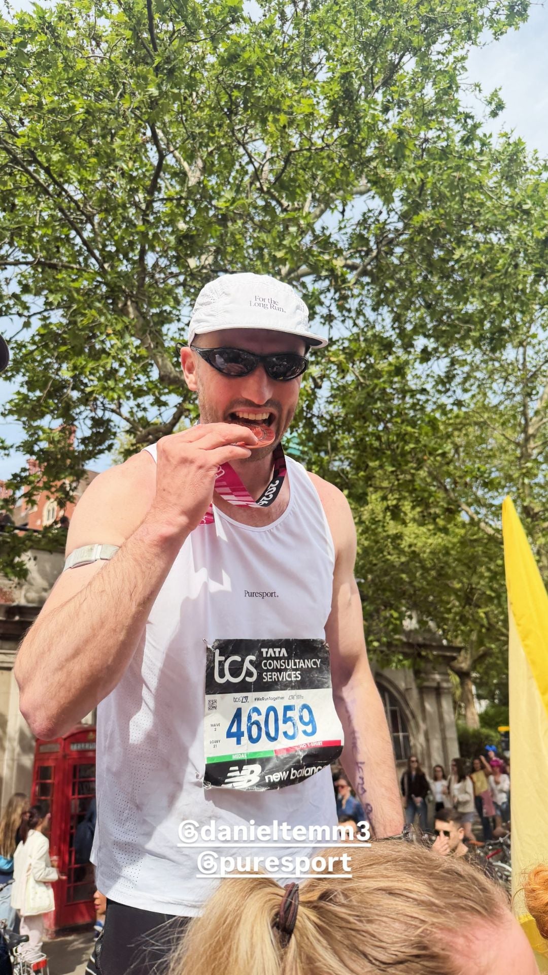 Man in a white tank Puresport singlet with a race number eating his marathon race medal. 