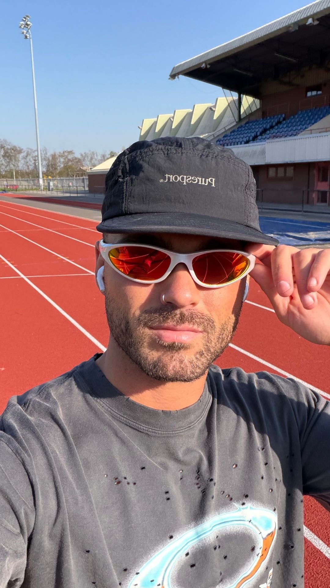 Man wearing sunglasses and a Puresport cap on a track field. 
