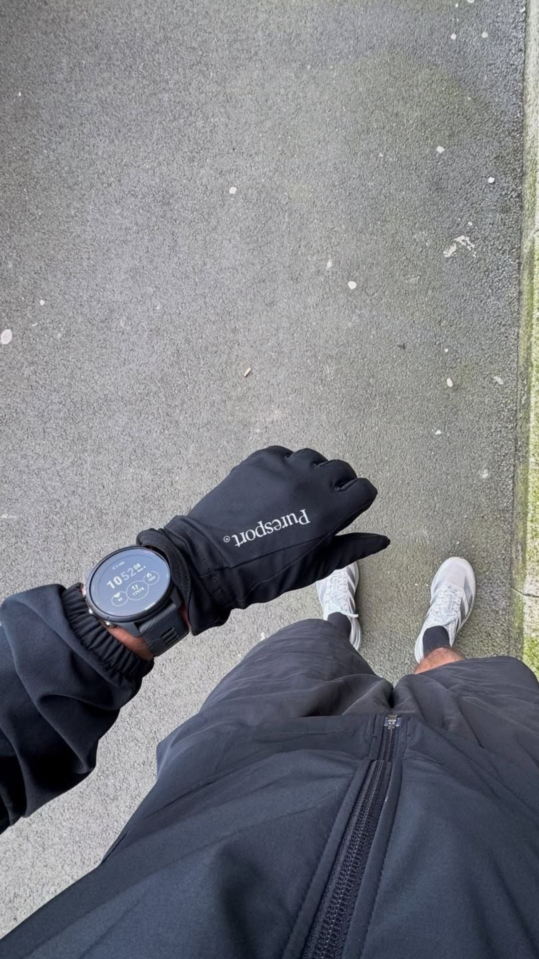 Runner wearing a black glove and garmin on the pavement