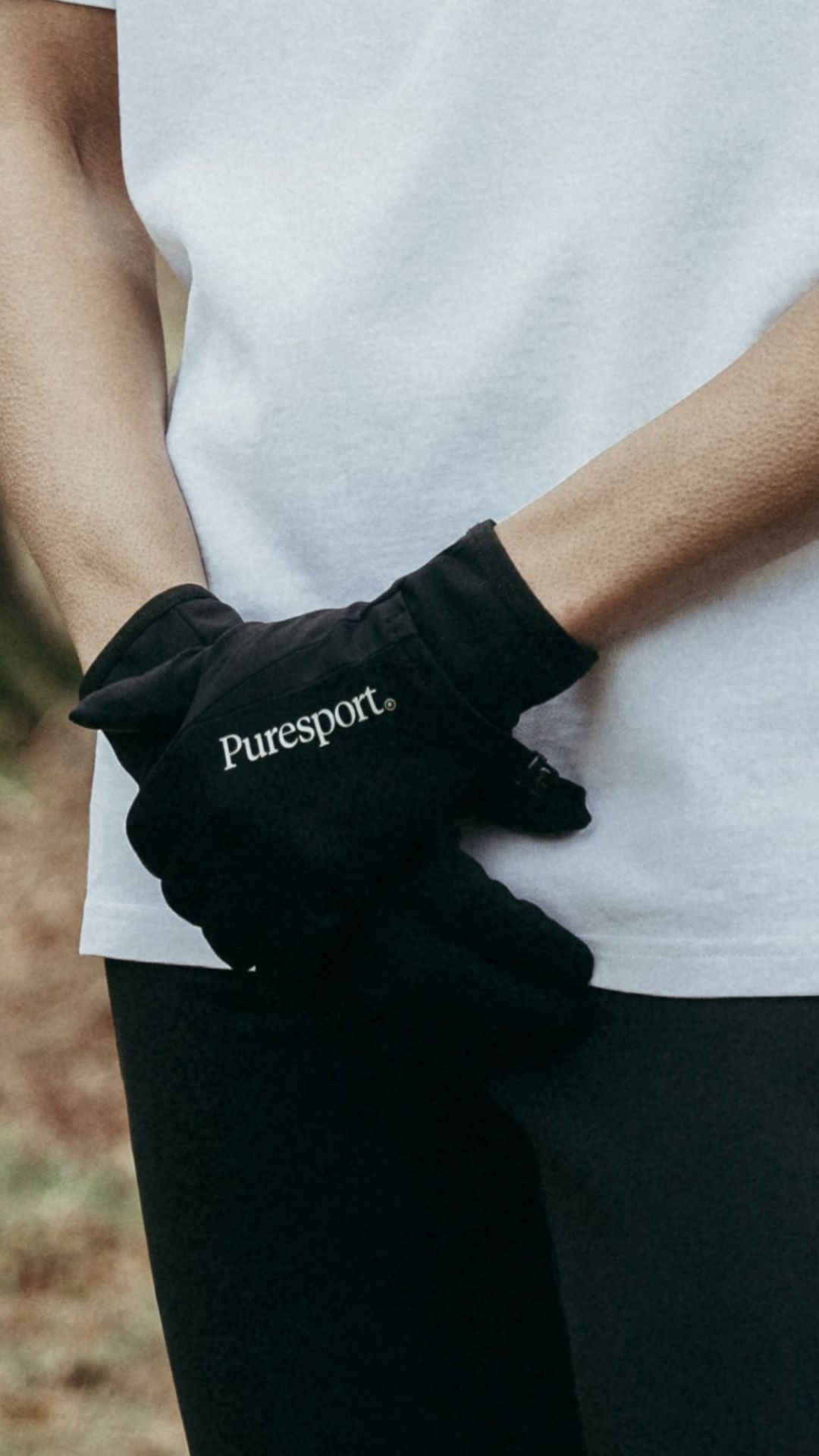 Person wearing black gloves with 'Puresport' logo, holding hands behind back.