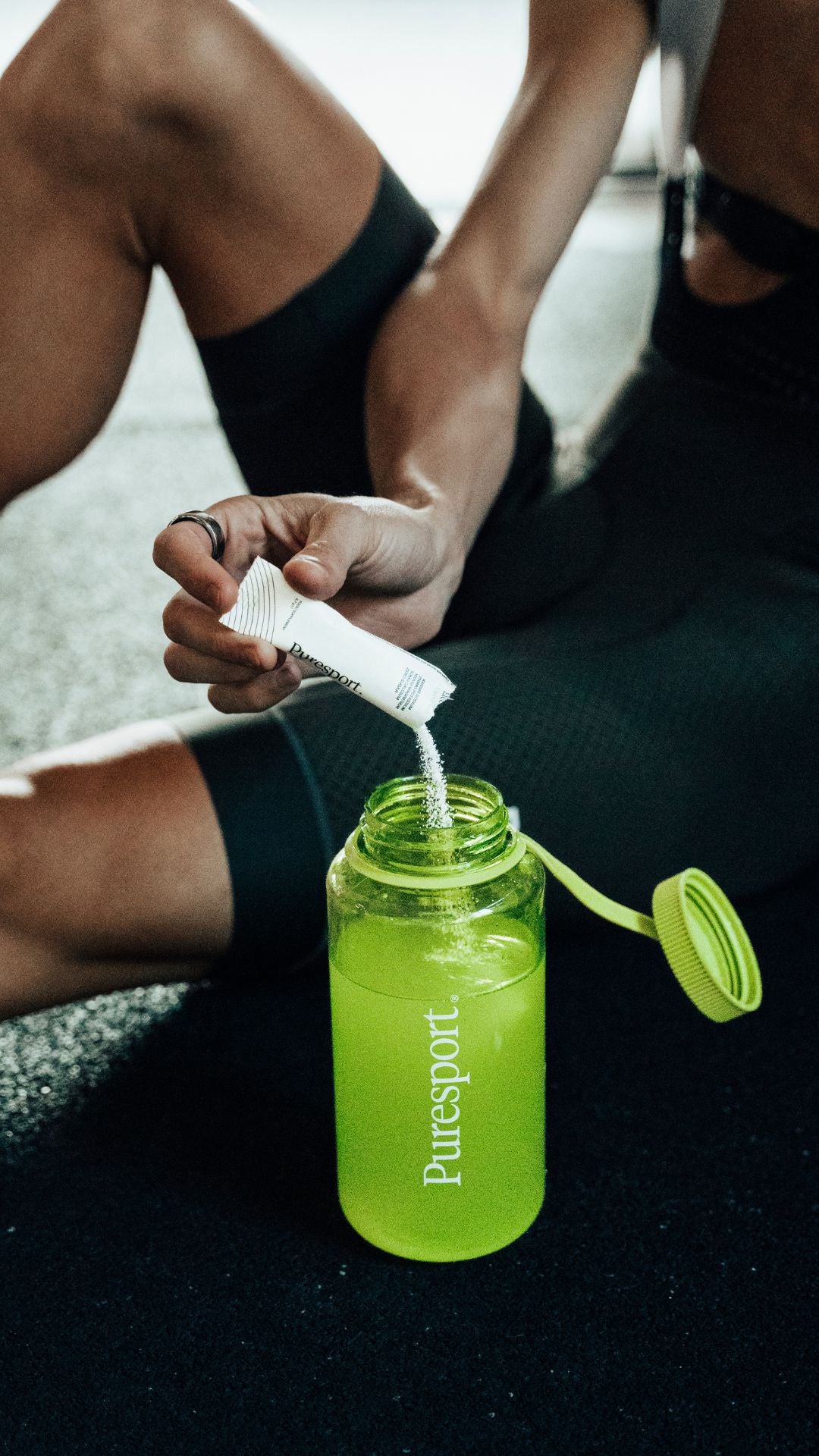 Person using a green Puresport water bottle with a straw on a blurred outdoor background swear cycling bibs