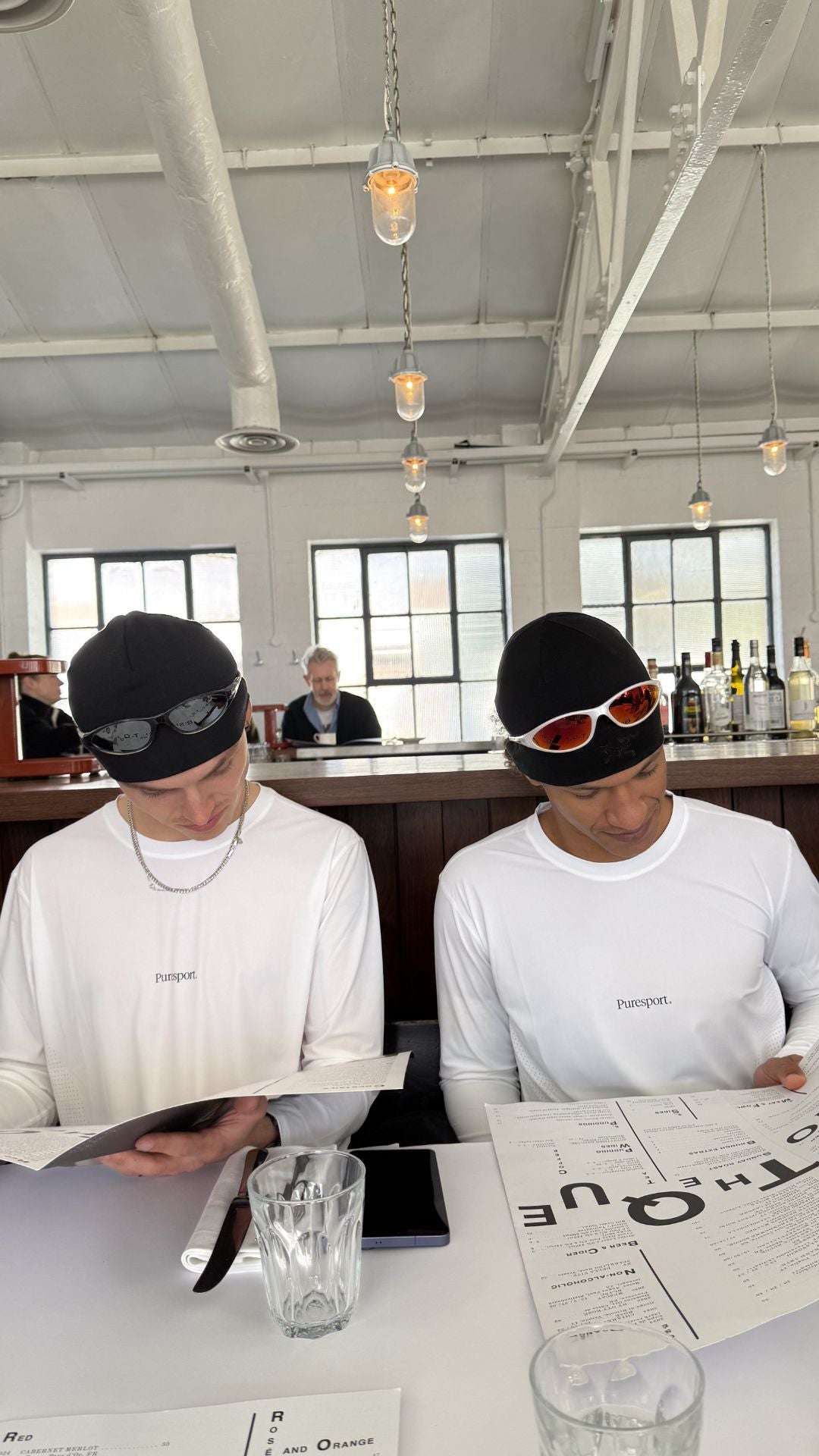 Two influencers sitting at a table with a menu, wearing Puresport running gera and AIM sunglasses.
