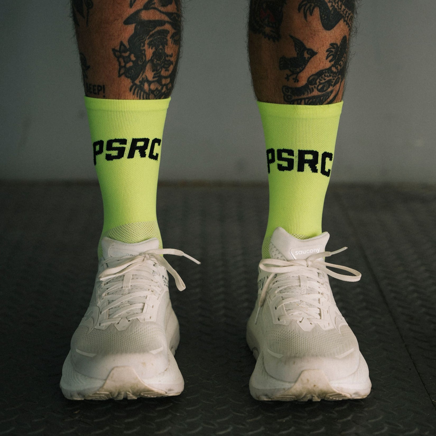 Person wearing bright green socks with 'PSRC' branding and white sneakers on a dark textured floor.
