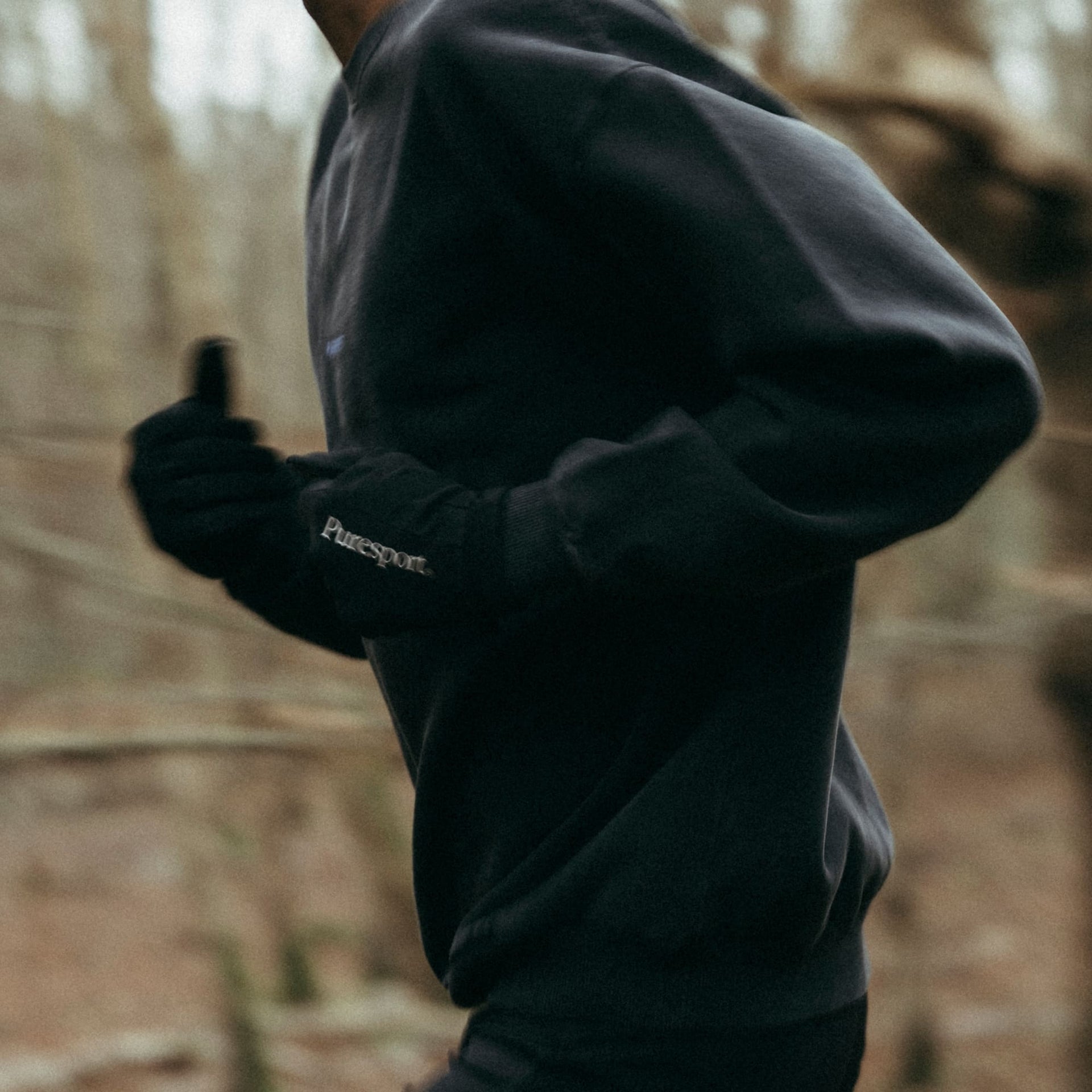 Person running in a black sweatshirt with 'Puresport' branding in a forest setting