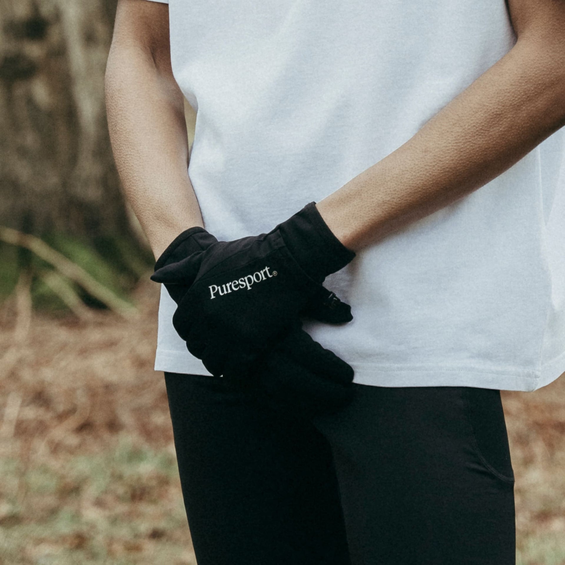 Person wearing a black glove with 'Puresport' branding, standing outdoors.