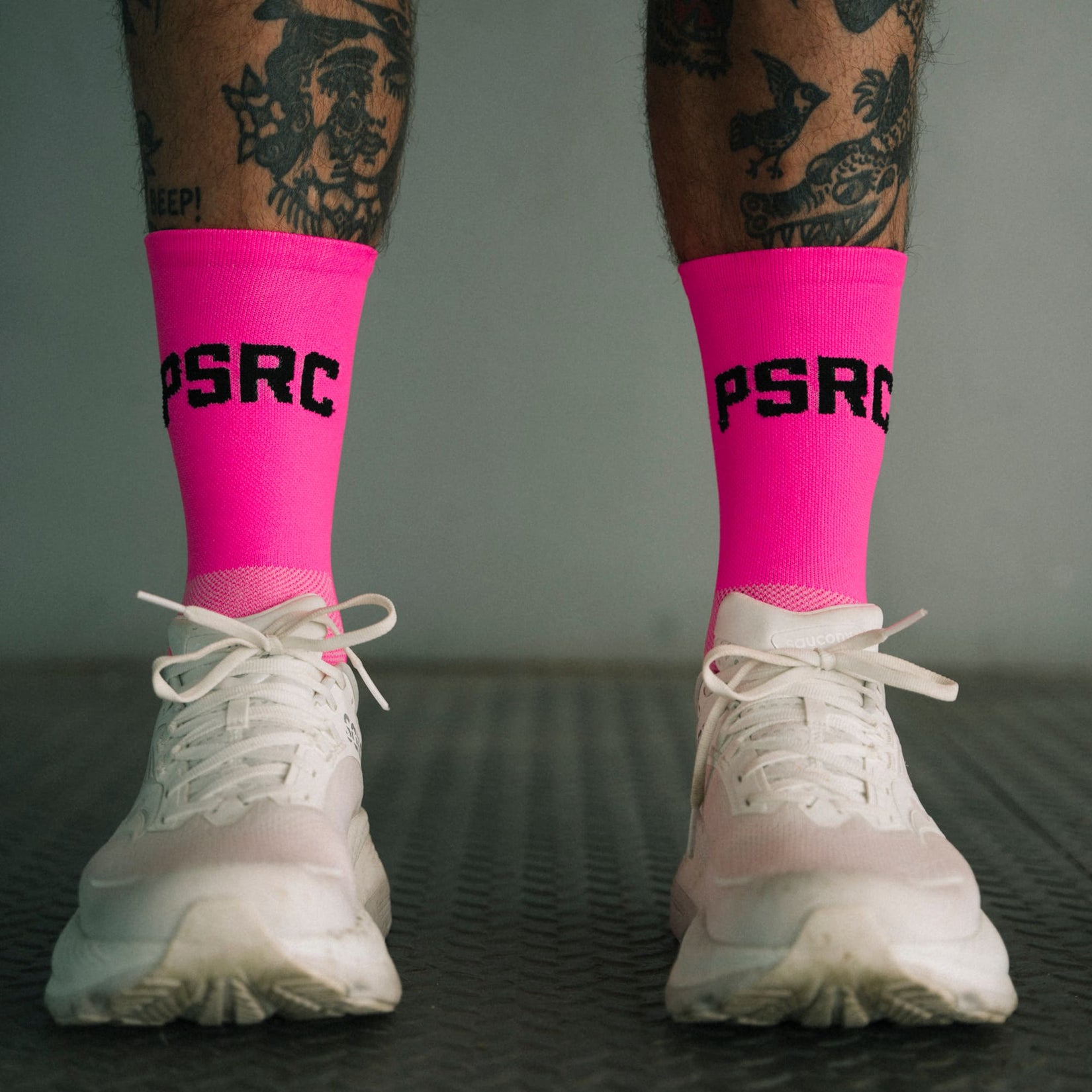 Person wearing pink socks with 'PSRC' logo and white sneakers on a dark surface.