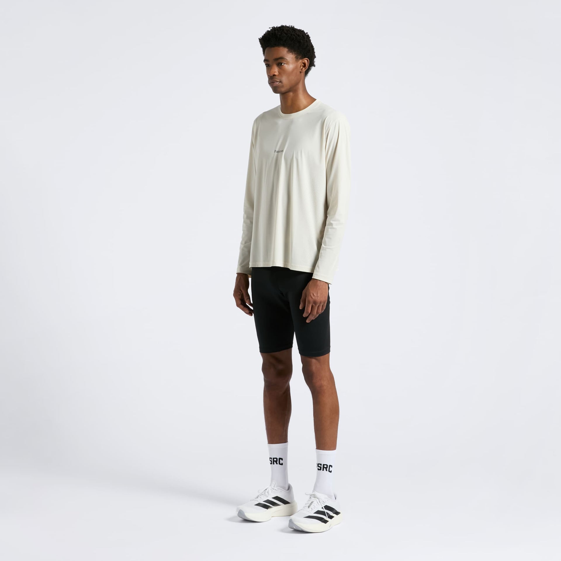 Person wearing a Sand long-sleeve shirt, black run shorts, and white sneakers and PSRC socks on a white background
