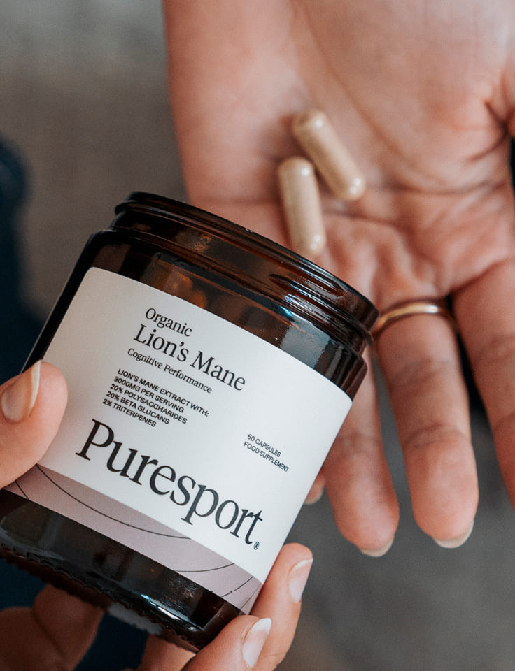 Jar of Puresport Organic Lion's Mane supplement held by a person.