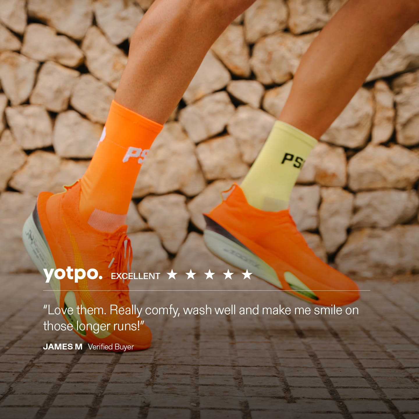 Runner wearing orange running shoes and socks with a stone wall background