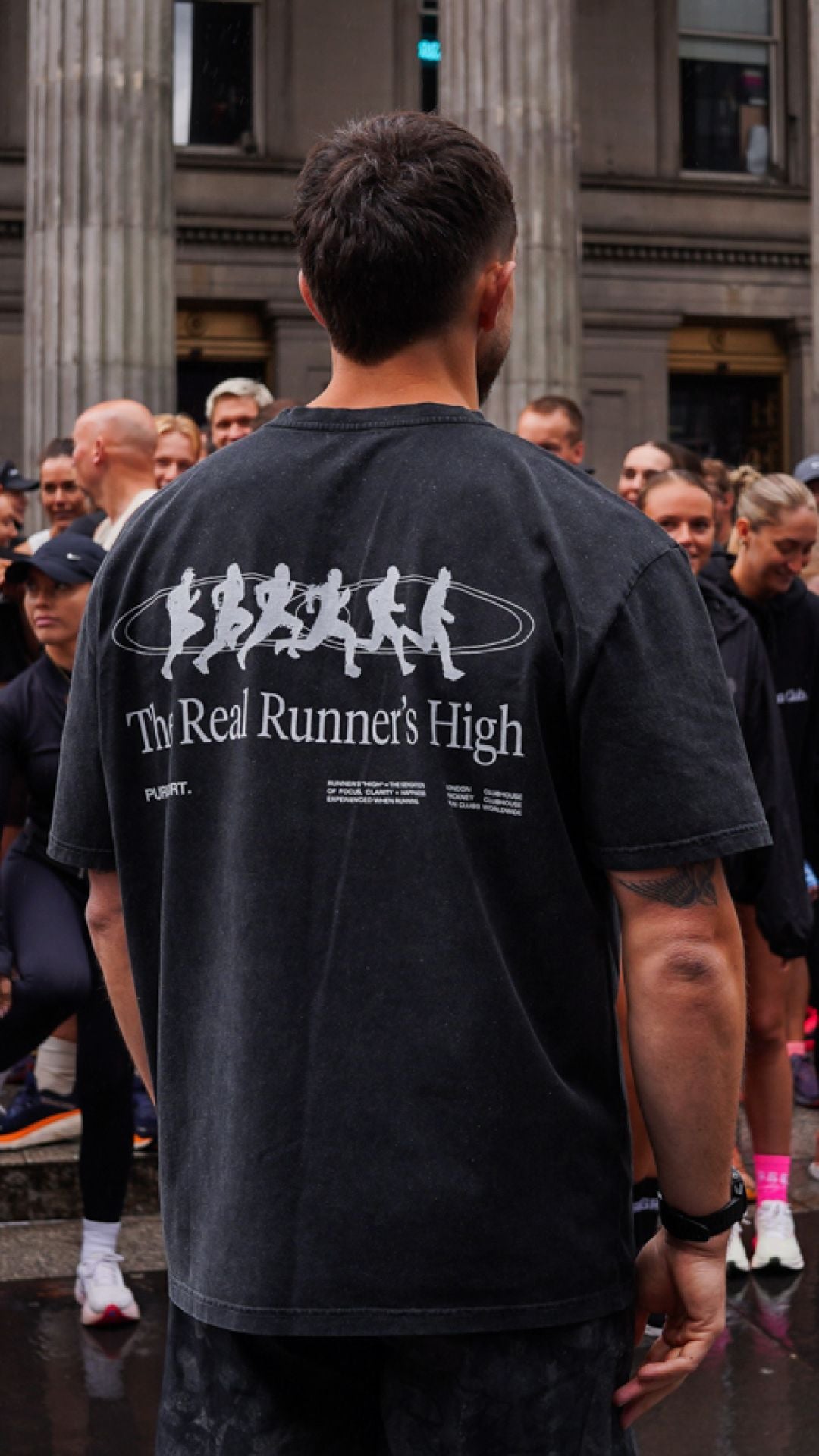 Male runner wearing a black t-shirt with 'The Real Runner's High' text and graphic at a run club. 