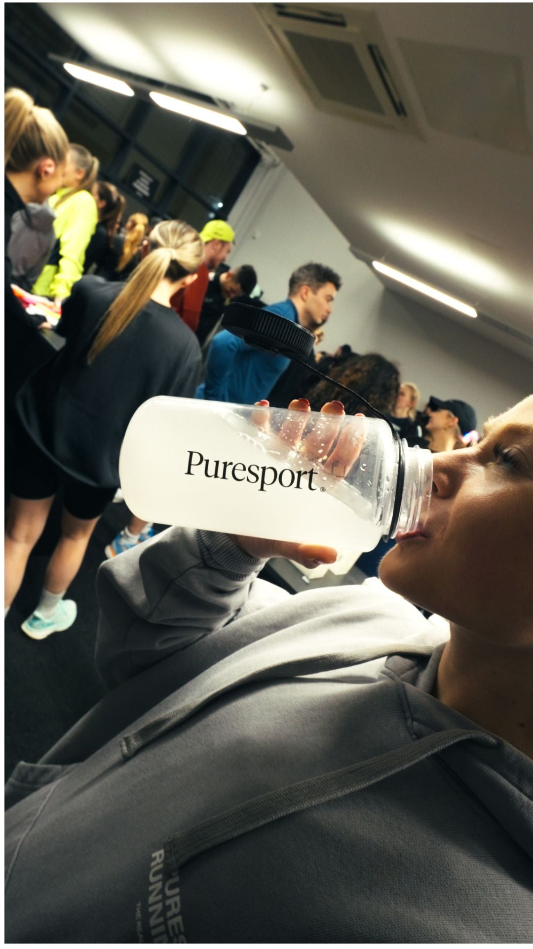 Person drinking from a Puresport water bottle in a crowded run club event. 