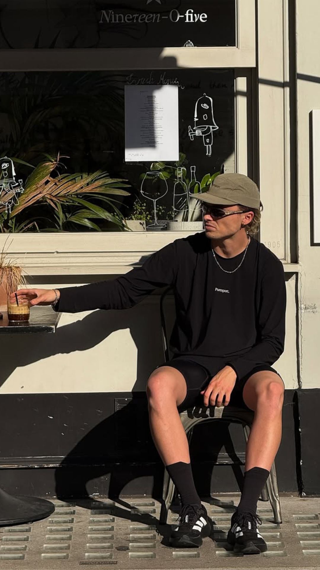 Runner sitting outdoors in front of a cafe with wearing Puresport running gear and AIM sunglasses. 