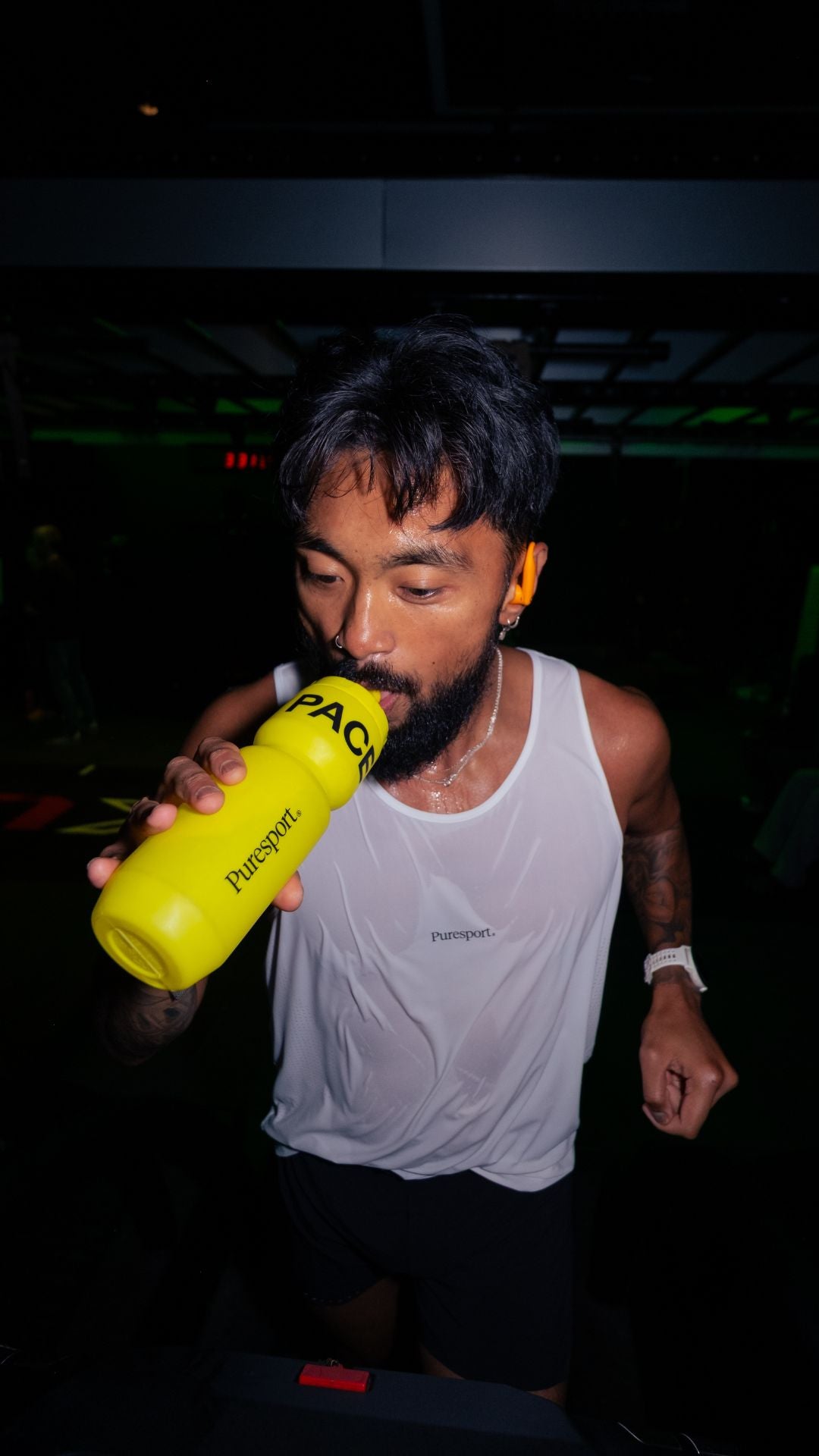 Sweaty runner drinking from a yellow bottle by Puresport with a dark background 