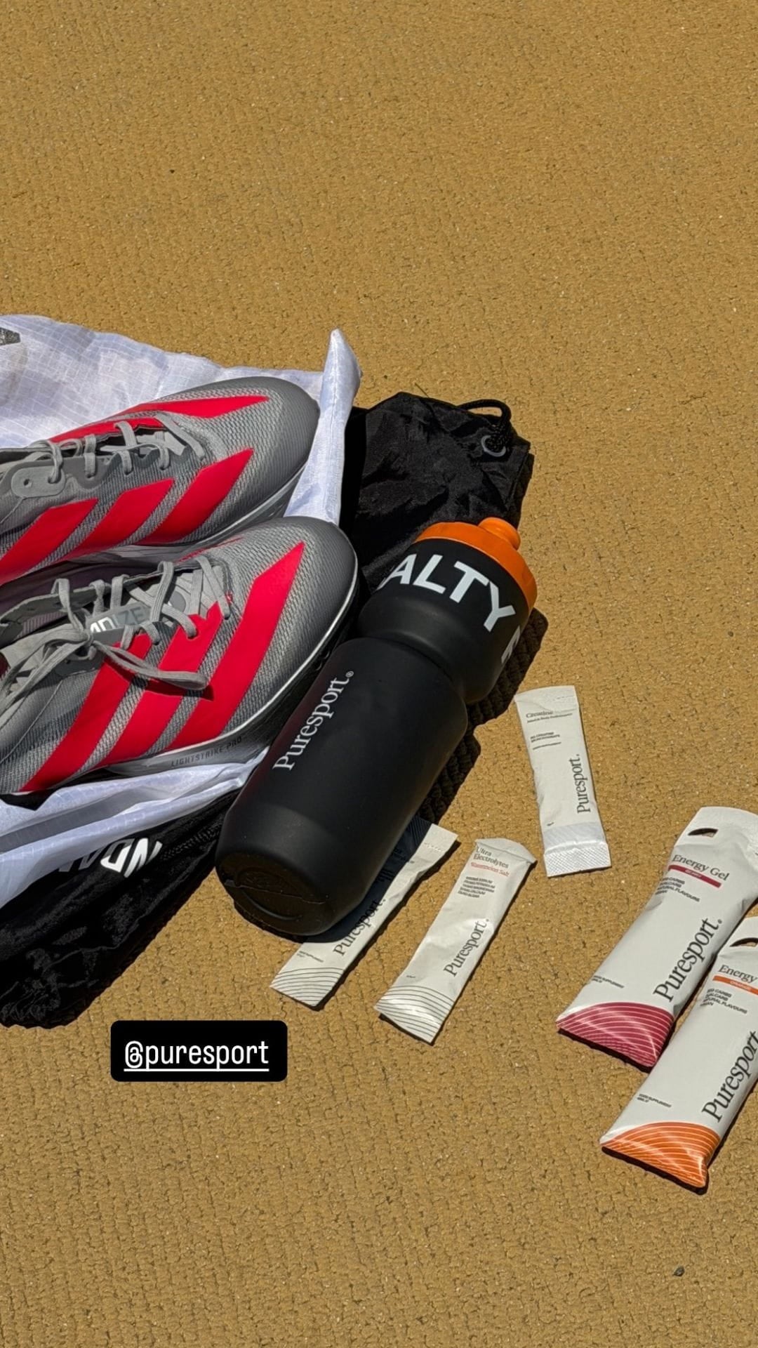 Sports shoes, water bottle, and energy gels on a sand with 'puresport' branding.