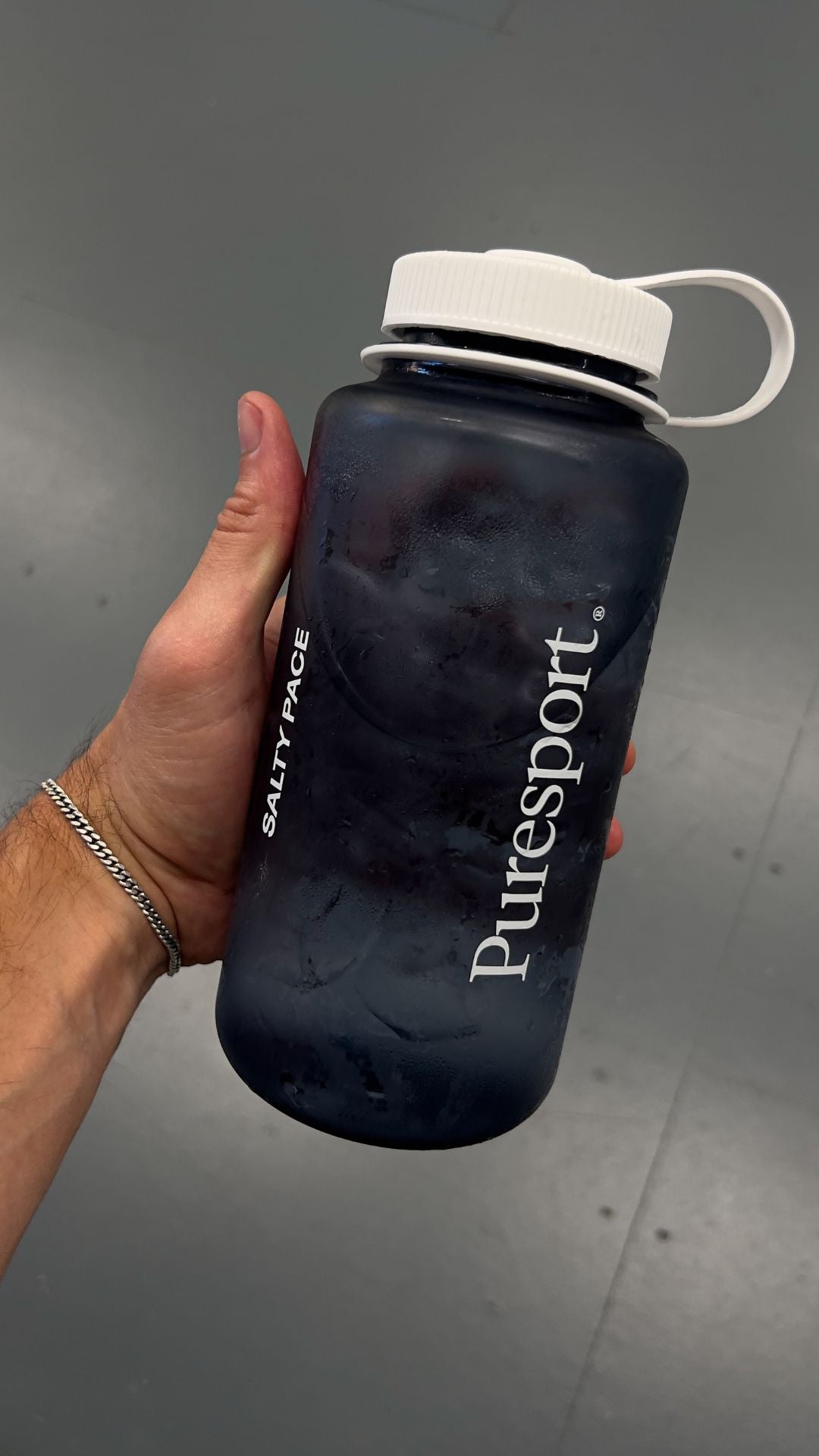 Smoke grey water bottle with white cap held by a hand on a gray background