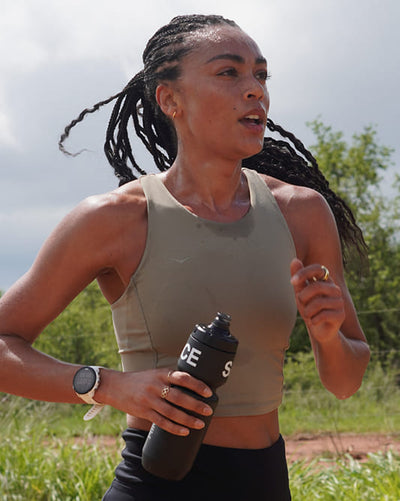 Woman running outdoors holding a Puresport sports water bottle. 
