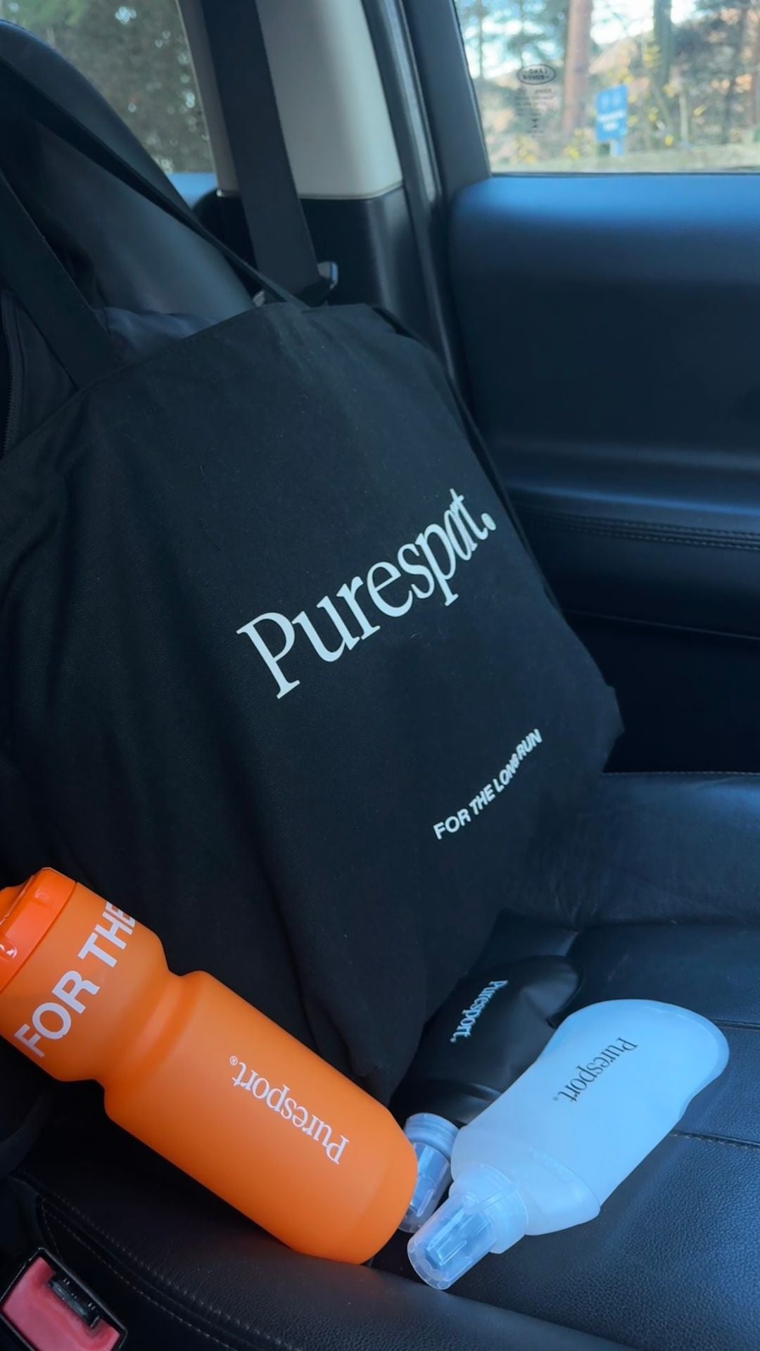Puresport products including a black towel, orange bottle, and clear water flask on a car seat.
