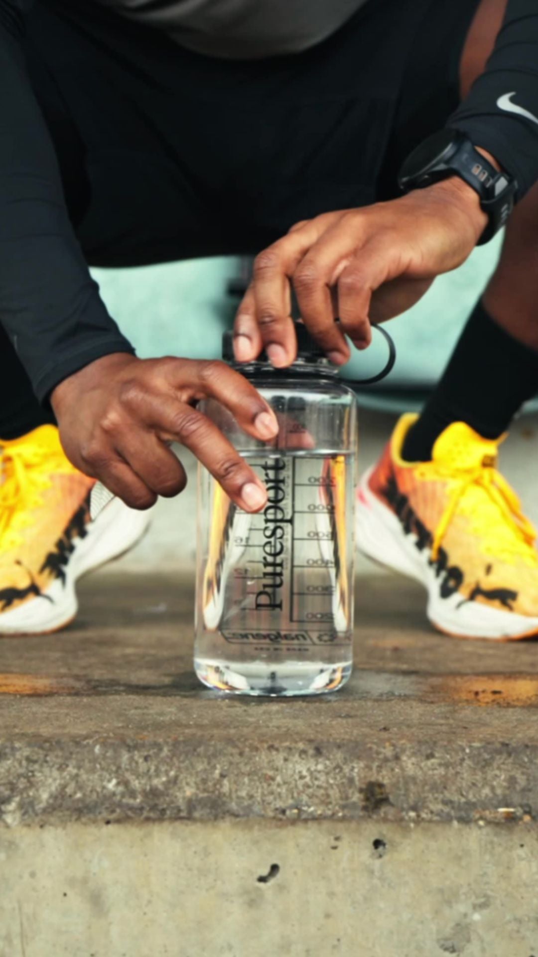 Athlete holding a clear water bottle labeled 'Puresport' on a concrete surface.