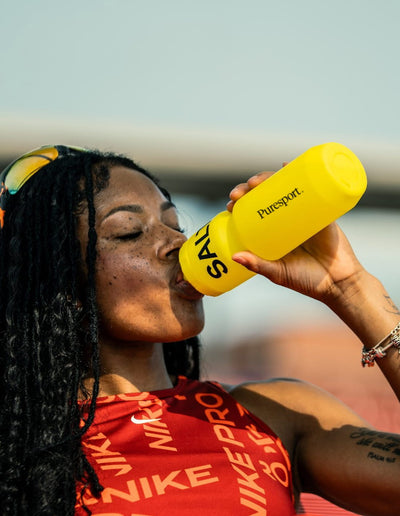 Athlete drinking from a yellow salty pace bottle with 'Puresport' branding, wearing a red Nike tank top.