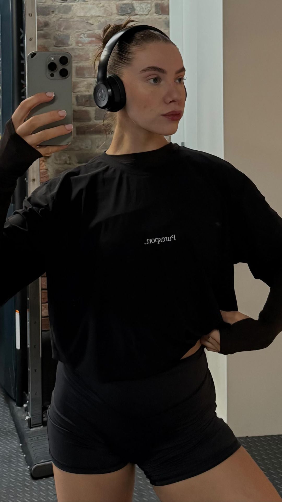 Person wearing a black Puresport top with and black shorts, taking a mirror selfie at the gym. 