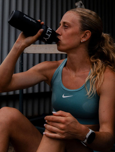 Woman in athletic wear drinking from a black water bottle with 'Puresport' branding.