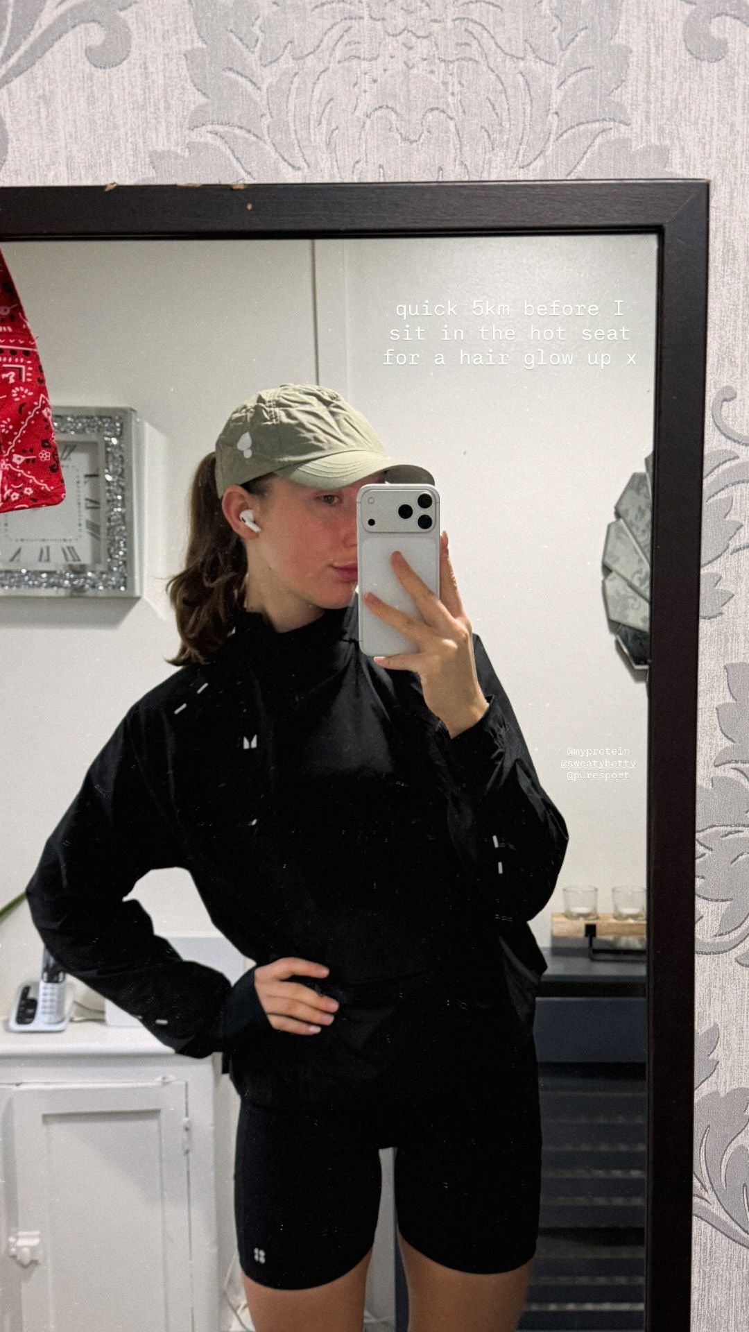 Person taking a mirror selfie wearing a black jacket and shorts indoors.
