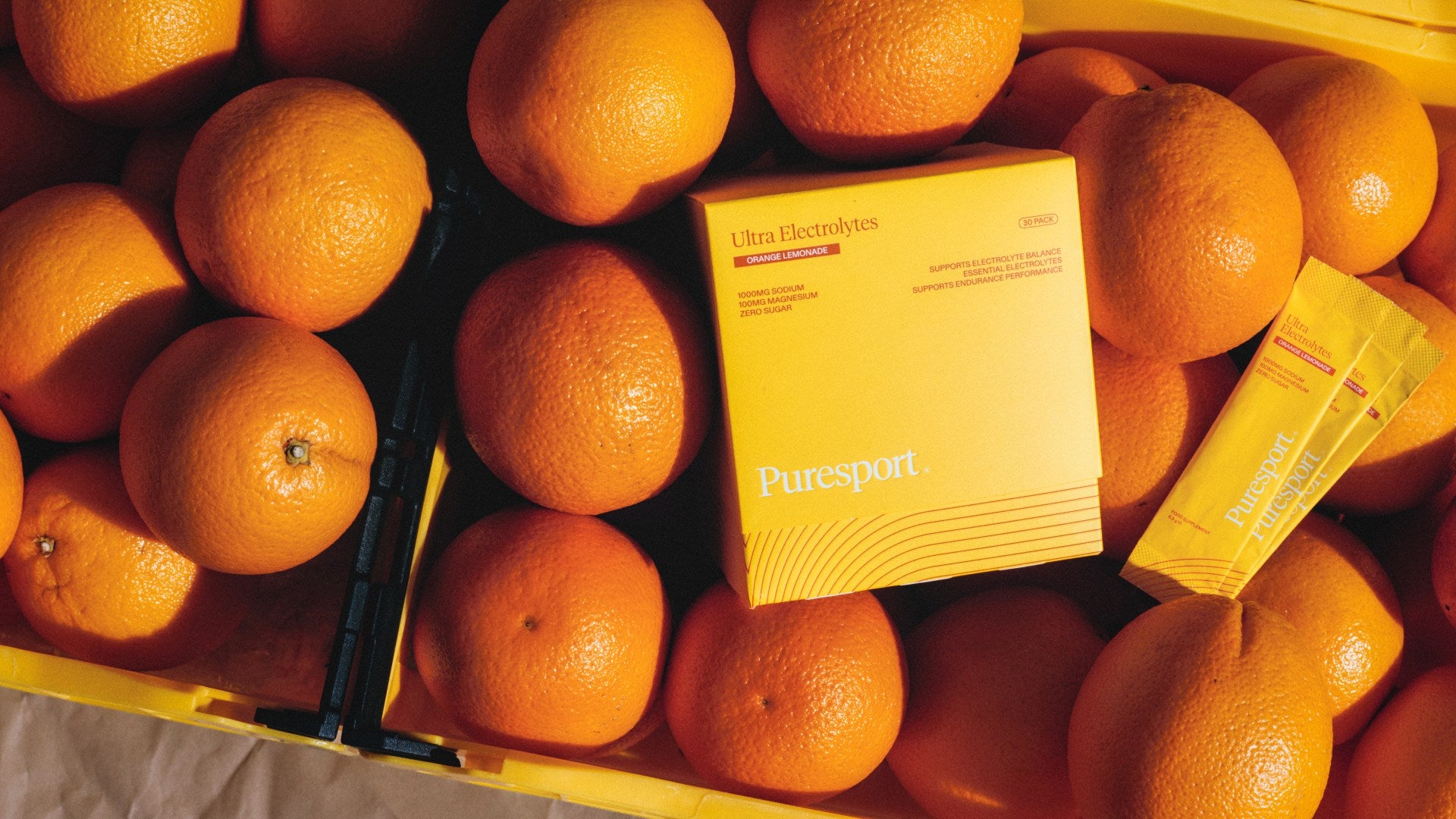 Puresport Ultra Electrolytes Orange Lemonade box and sachet among fresh oranges